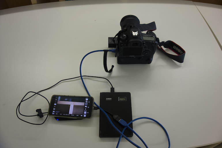A camera connected to a cell phone, external battery, and Qi pad.
